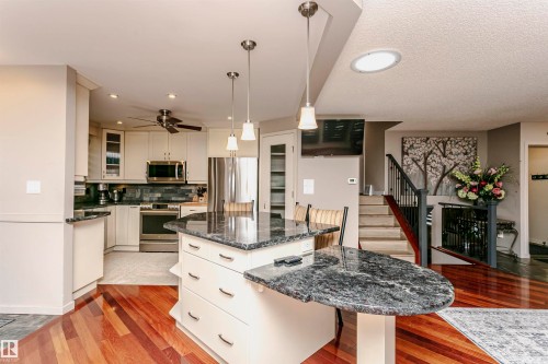 The kitchen features a dark granite island with pendant lighting, stainless steel appliances, and cream cabinetry, complemented by rich hardwood flooring - 9831 185 Street, Edmonton, AB - Indoor Photo Showing Kitchen With Upgraded Kitchen