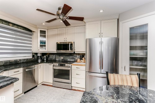 The kitchen features light-colored cabinetry, stainless steel appliances, dark granite countertops, and a stone-tiled backsplash - 9831 185 Street, Edmonton, AB - Indoor Photo Showing Kitchen
