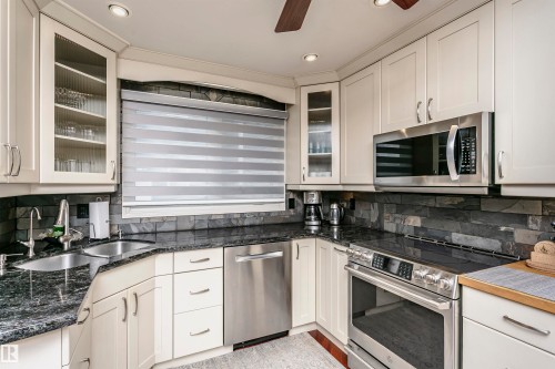 This kitchen features white cabinetry with glass-front accents, dark granite countertops, and a stone-tiled backsplash - 9831 185 Street, Edmonton, AB - Indoor Photo Showing Kitchen With Double Sink With Upgraded Kitchen