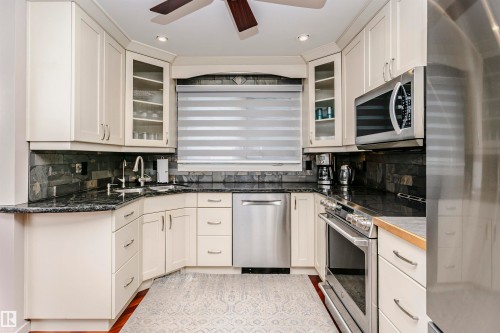Well-appointed kitchen featuring light-colored cabinetry, dark countertops, and stainless steel appliances including a microwave, oven, and dishwasher - 9831 185 Street, Edmonton, AB - Indoor Photo Showing Kitchen With Upgraded Kitchen