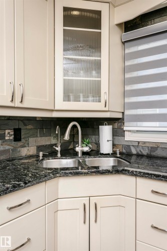 The kitchen features cream-colored cabinetry with brushed nickel hardware, a corner stainless steel double sink, and dark granite countertops - 9831 185 Street, Edmonton, AB - Indoor Photo Showing Kitchen