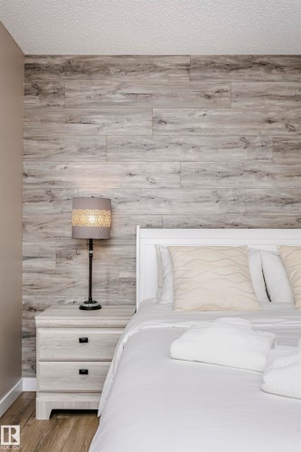 This bedroom features a stylish wood plank accent wall, a white bed frame, and a nightstand with two drawers - 9831 185 Street, Edmonton, AB - Indoor Photo Showing Other Room