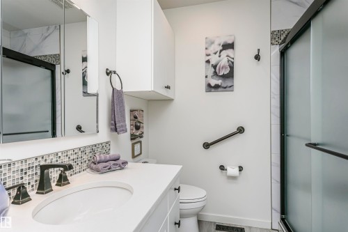 The bathroom features a vanity with a white countertop and an undermount sink, accented by dark bronze fixtures and a mosaic tile backsplash - 9831 185 Street, Edmonton, AB - Indoor Photo Showing Bathroom