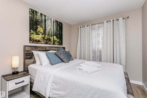 Bedroom featuring light-colored walls, a bed with a wooden headboard, and a nightstand with a lamp - 9831 185 Street, Edmonton, AB - Indoor Photo Showing Bedroom