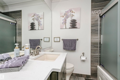Well-appointed bathroom featuring a vanity with a white countertop and an integrated sink, a brushed nickel faucet, and a shower with frosted glass doors and tiled surround - 9831 185 Street, Edmonton, AB - Indoor Photo Showing Bathroom
