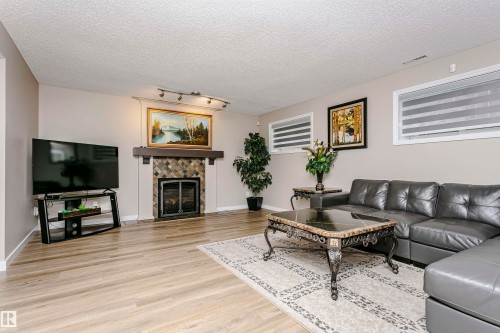 Living room featuring light-toned flooring, a fireplace with a stone facade and dark mantel, and recessed windows with horizontal blinds - 9831 185 Street, Edmonton, AB - Indoor Photo Showing Living Room With Fireplace
