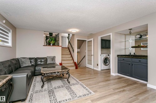 Living area featuring light wood-style flooring, a staircase with dark railings, and a built-in cabinet with a dark countertop - 9831 185 Street, Edmonton, AB - Indoor Photo Showing Living Room