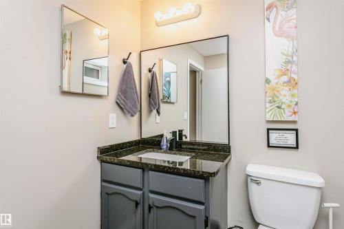 The bathroom features a vanity with a dark countertop and a white sink, a mirror with a black frame, and a white toilet - 9831 185 Street, Edmonton, AB - Indoor Photo Showing Bathroom