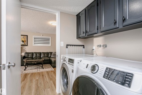 Laundry area featuring gray cabinetry and a view into a living space with light wood flooring - 9831 185 Street, Edmonton, AB - Indoor Photo Showing Laundry Room