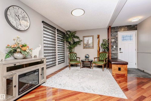 The property features hardwood flooring, a large area rug, and a front entry door with decorative glass - 9831 185 Street, Edmonton, AB - Indoor Photo Showing Other Room With Fireplace