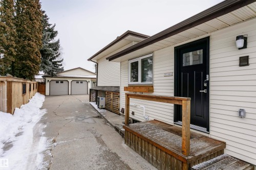 The property features a white exterior, a black entry door with a glass insert, and a wooden front deck with a railing - 9831 185 Street, Edmonton, AB - Outdoor With Exterior
