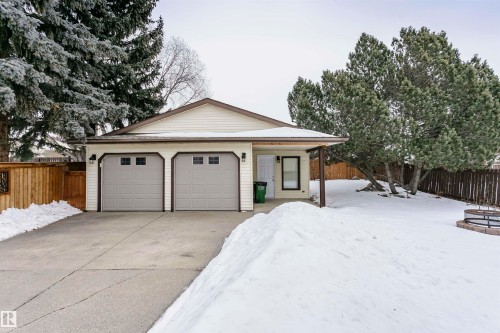 The property features a two-car garage with overhead doors, a paved driveway, and a fenced yard with mature trees - 9831 185 Street, Edmonton, AB - Outdoor