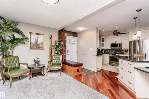 The open concept living area features rich hardwood flooring and leads into a kitchen with white cabinetry, stainless steel appliances, and dark countertops - 9831 185 Street, Edmonton, AB - Indoor Photo Showing Kitchen With Upgraded Kitchen