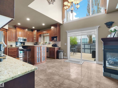 Open-concept kitchen and living area featuring a vaulted ceiling with high windows, an integrated fireplace, and direct access to an exterior deck - 1511 69 Street, Edmonton, AB - Indoor Photo Showing Kitchen