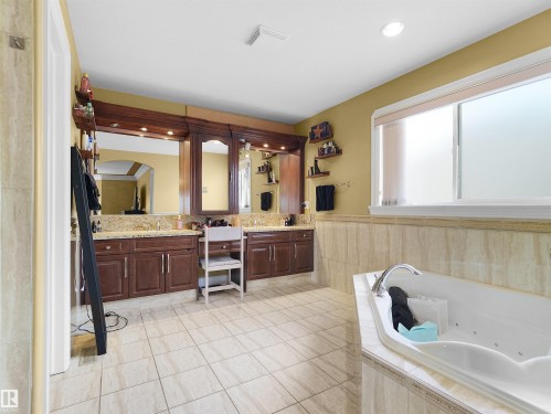 Spacious bathroom with a jetted soaking tub, dual vanity with granite countertops, rich wood cabinetry, and tiled flooring - 1511 69 Street, Edmonton, AB - Indoor Photo Showing Bathroom