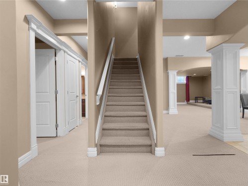 Carpeted staircase with white railings, leading to an expansive lower level featuring cream-colored carpeting, white trim, recessed lighting, and decorative white columns - 1511 69 Street, Edmonton, AB - Indoor Photo Showing Other Room