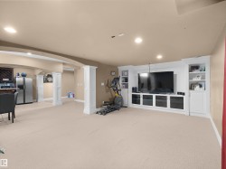 Spacious entertainment area featuring a built-in media center with shelving, recessed lighting, carpeted flooring, and architectural columns - 
