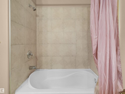 Bathtub and shower combination featuring neutral-toned wall tiling, chrome showerhead, and coordinating chrome fixtures - 1511 69 Street, Edmonton, AB - Indoor Photo Showing Bathroom