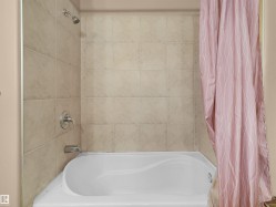 Bathtub and shower combination featuring neutral-toned wall tiling, chrome showerhead, and coordinating chrome fixtures - 