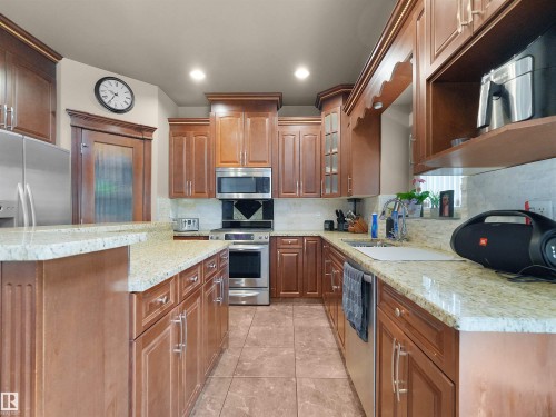 Kitchen featuring extensive wood cabinetry, light-toned countertops, stainless steel appliances, and tiled flooring - 1511 69 Street, Edmonton, AB - Indoor Photo Showing Kitchen
