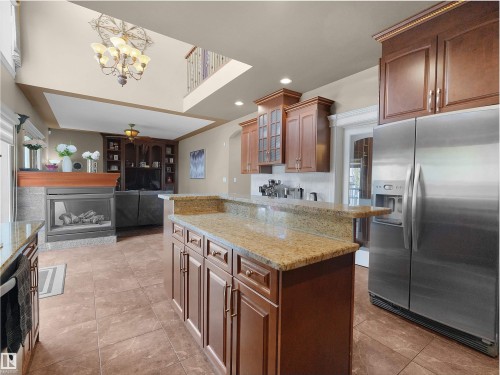 Kitchen island with granite countertops, rich wood cabinetry, and a stainless steel refrigerator - 1511 69 Street, Edmonton, AB - Indoor Photo Showing Kitchen With Fireplace
