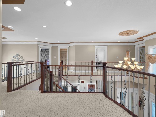 Spacious upper-level landing featuring patterned carpet, dark wood railings with decorative iron balusters, recessed lighting, and a prominent chandelier with an ornate ceiling medallion - 1511 69 Street, Edmonton, AB - Indoor Photo Showing Other Room