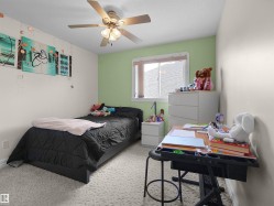Bedroom featuring a ceiling fan with integrated lighting, a window with blinds, light-toned walls with a contrasting accent wall, and patterned carpeting - 
