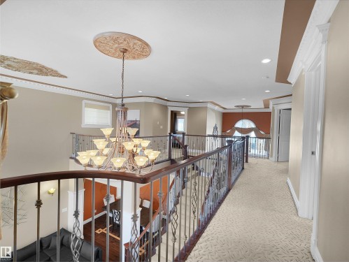 Grand upper-level landing featuring a large multi-tier chandelier, ornate ceiling medallions, decorative wrought iron railings with wood-finish handrails, recessed lighting, and patterned carpeting - 1511 69 Street, Edmonton, AB - Indoor Photo Showing Other Room