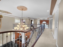 Grand upper-level landing featuring a large multi-tier chandelier, ornate ceiling medallions, decorative wrought iron railings with wood-finish handrails, recessed lighting, and patterned carpeting - 