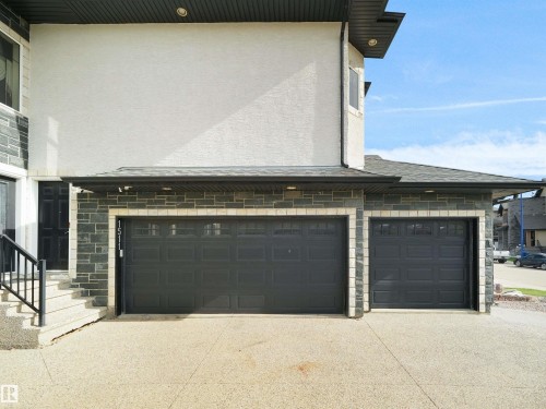 Three-car garage with two dark panel doors and transom windows, complemented by a stone facade - 1511 69 Street, Edmonton, AB - Outdoor With Exterior