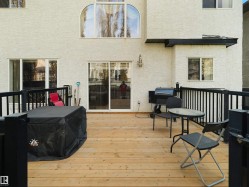 Spacious wood deck with black metal railings, white stucco exterior, sliding glass door access, and an arched window feature - 