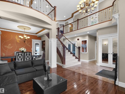 Two-story foyer featuring a grand staircase with wrought iron balusters, wood-finish flooring, and an elegant chandelier - 1511 69 Street, Edmonton, AB - Indoor Photo Showing Living Room