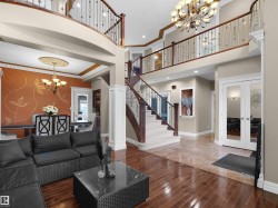 Two-story foyer featuring a grand staircase with wrought iron balusters, wood-finish flooring, and an elegant chandelier - 