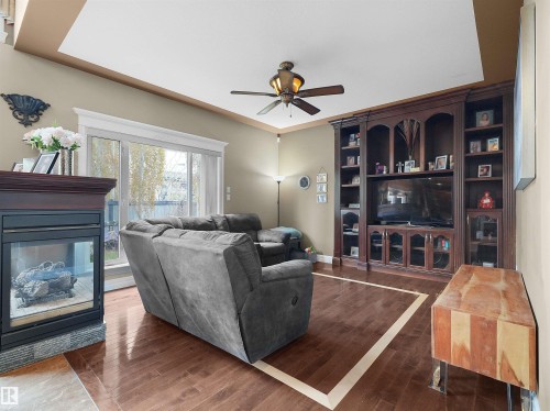 Living area featuring wood-finish flooring with a light wood inlay detail, a built-in entertainment center, and a gas fireplace with a dark wood mantle - 1511 69 Street, Edmonton, AB - Indoor Photo Showing Living Room With Fireplace