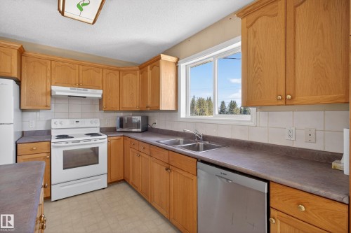 Kitchen featuring wood cabinetry, laminate countertops, a dual basin stainless steel sink, and a white tile backsplash - 5204 55 Ave, Mundare, AB - Indoor Photo Showing Kitchen With Double Sink