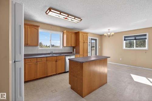 Kitchen featuring wood-finish cabinetry, a central island, a white tile backsplash, and durable laminate countertops - 5204 55 Ave, Mundare, AB - Indoor Photo Showing Kitchen With Double Sink