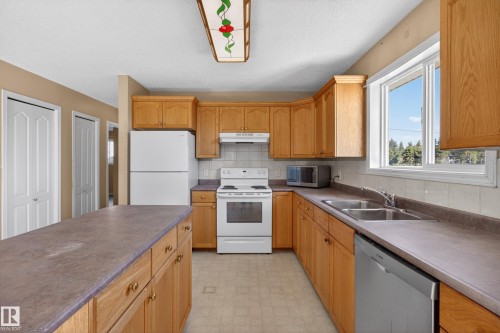 Kitchen with light wood cabinetry, white appliances, and a double basin stainless steel sink - 5204 55 Ave, Mundare, AB - Indoor Photo Showing Kitchen With Double Sink