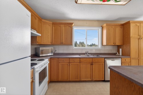 Kitchen featuring wood cabinetry, white appliances, and a double basin sink - 5204 55 Ave, Mundare, AB - Indoor Photo Showing Kitchen With Double Sink