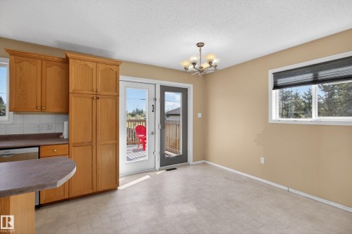Dining space featuring a chandelier, wood-finish cabinetry, a window with roller blind, and patio doors leading to a deck - 5204 55 Ave, Mundare, AB - Indoor Photo Showing Other Room