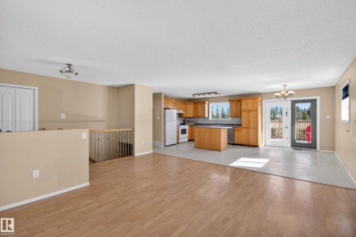 Open-concept living space featuring wood-finish flooring, a kitchen with light wood cabinetry, a center island, and white appliances - 5204 55 Ave, Mundare, AB - Indoor