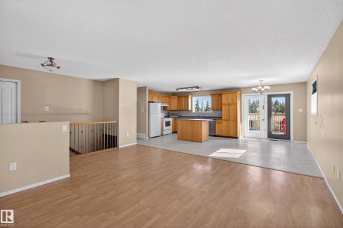 Open concept living area featuring wood-finish flooring, a kitchen with light wood cabinetry, an island, and a dining area with a glass-paneled door - 5204 55 Ave, Mundare, AB - Indoor