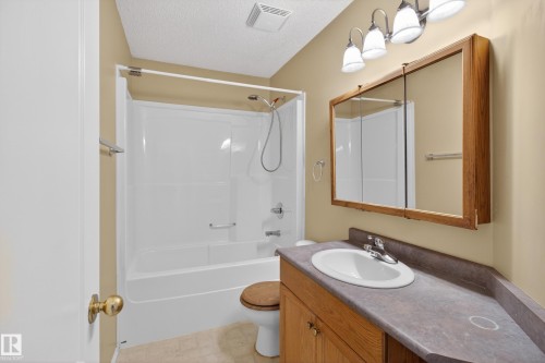 Full bathroom featuring a white tub/shower combination, oak vanity with an integrated sink and laminate countertop, and a framed medicine cabinet with mirrored doors - 5204 55 Ave, Mundare, AB - Indoor Photo Showing Bathroom