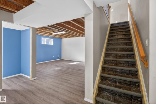 Staircase featuring dark patterned risers and treads with a light wood handrail - 5204 55 Ave, Mundare, AB - Indoor Photo Showing Other Room