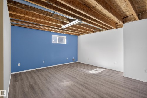 Spacious unfinished basement offering exposed ceiling joists, wood-finish flooring, white and blue painted walls, and a small egress window - 5204 55 Ave, Mundare, AB - Indoor Photo Showing Basement