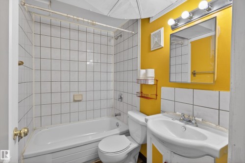 Bathroom featuring a white subway tile tub surround, white bathtub, and a wall-mounted sink with a vanity mirror above - 5204 55 Ave, Mundare, AB - Indoor Photo Showing Bathroom