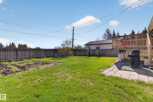 Expansive backyard featuring a manicured lawn, a wooden privacy fence, a raised wood deck, a paved patio, and a garden area - 5204 55 Ave, Mundare, AB - Outdoor