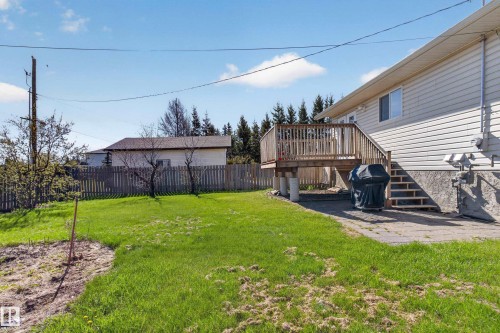 Rear exterior showcasing an elevated wood deck with railing and stairs, vinyl siding, and a partial concrete patio - 5204 55 Ave, Mundare, AB - Outdoor