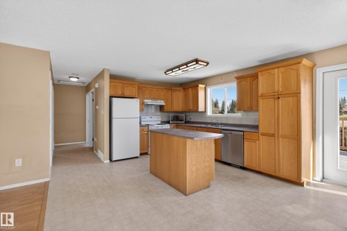 Open-concept kitchen featuring wood cabinetry, an island with countertop, and a white appliance package - 5204 55 Ave, Mundare, AB - Indoor Photo Showing Kitchen