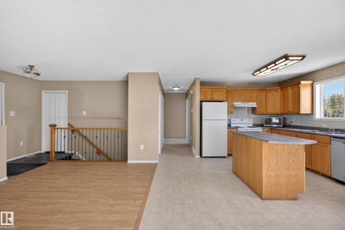 Open-concept kitchen and living area featuring wood-finish flooring, a central kitchen island with countertop, natural wood cabinetry, and stainless-steel appliances - 5204 55 Ave, Mundare, AB - Indoor Photo Showing Kitchen