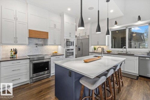 Spacious kitchen featuring an expansive island with seating, stainless steel appliances, abundant white cabinetry, wood-finish flooring, and a vaulted ceiling - 10611 146 Street Nw, Edmonton, AB - Indoor Photo Showing Kitchen With Upgraded Kitchen